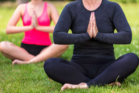 Anonymous mature fit healthy middle aged female yoga teacher yogi teaching young woman at yoga practice outside in a natural tranquil green environmentの写真素材