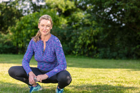 Outdoor portrait of an attractive middle aged blonde woman smiling drinking water relaxing after exercising, running or fitness lifestyleの写真素材
