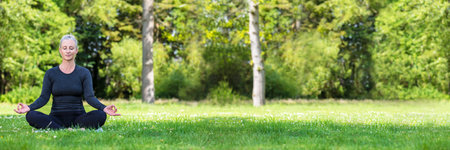 Panoramic web banner of mature middle aged fit healthy woman practicing yoga outsidein a natural tranquil green environment panorama.の写真素材