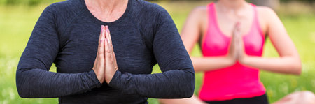 Panorama anonymous mature fit healthy middle aged female yoga teacher yogi teaching young woman at yoga practice outside in a natural tranquil green environment panoramic web bannerの写真素材