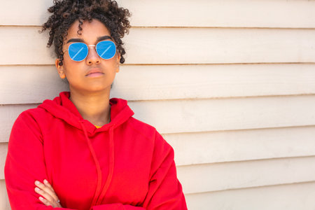 Girl teenager cool teen mixed race biracial African American female young woman wearing sunglasses reflecting aiplane in blue sky in summer sunshineの写真素材