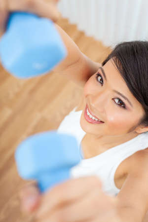 Beautiful Chinese Asian young woman or girl exercising with weightsblue dumb bells at home or in a gymの写真素材