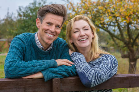 Attractive, successful and happy middle aged man and woman couple together outside leaning on a fence in the countrysideの写真素材