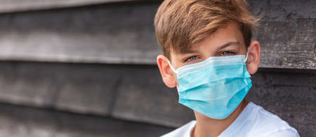 Panorama boy teenager teen male child wearing a face mask outside during the Coronavirus COVID-19 virus  pandemic panoramic web bannerの写真素材