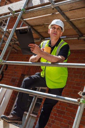 Male builder foreman, construction worker or architect on site holding a clipboard and drinking a mug of coffee or teaの写真素材