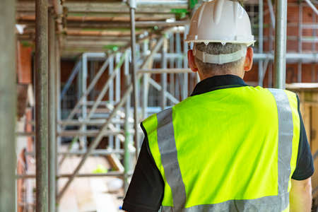 Rear view of male builder construction worker or builder on building site wearing hard hat and hi-vis vestの写真素材