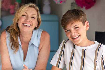 Teenage teen boy son laughing in a kitchen with his mother out of focus behind himの写真素材