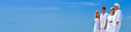 Panoramic web banner two couples, generations of a family together holding hands with a blue sky panoramaの写真素材