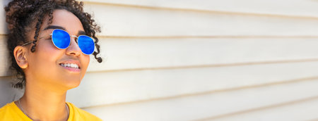 Panorama girl teenager cool teen mixed race biracial African American female young woman wearing blue sunglasses and a yellow t-shirt on vacation smiling in summer sunshine panoramic web bannerの写真素材