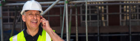 Panoramic web banner male builder, construction worker, contractor or architect on building site talking on his cell phone panoramic header