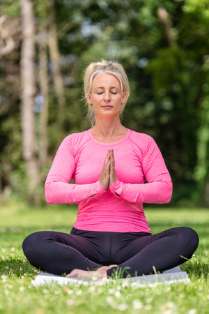 Mature middle aged fit healthy woman practicing yoga outside in a natural tranquil green environmentの写真素材