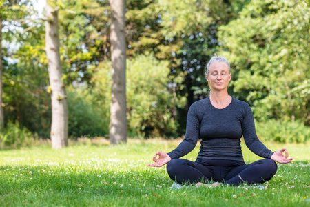 Mature middle aged fit healthy woman practicing yoga outsidein a natural tranquil green environmentの写真素材