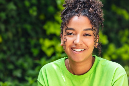 Outdoor portrait of beautiful happy mixed race biracial African American girl teenager female young woman smiling with perfect teeth wearing a green t-shirtの写真素材