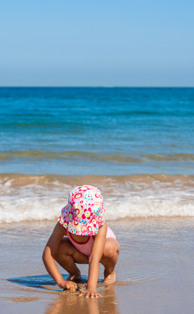 Cute little girl female child sitting playing on a beach on pink swimming costume and hatの写真素材