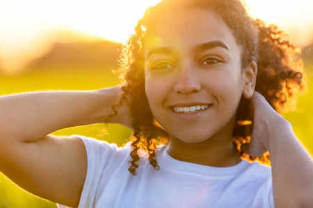Beautiful biracial mixed race African American teenager teen girl young woman smiling outside backlit at sunset or sunriseの写真素材