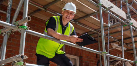 Panoramic web banner header of male builder foreman, construction worker, contractor or architect on building site writing on black clipboard panoramaの写真素材