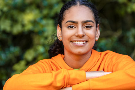 Outdoor portrait of beautiful happy mixed race African American girl teenager female young woman happy and smiling with perfect teeth with a natural green leaves backgroundの写真素材