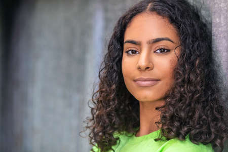 Outdoor portrait of beautiful happy mixed race African American girl teenager female young woman thinking and smiling with an urban city backgroundの写真素材