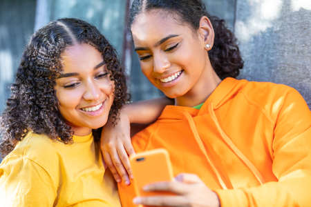 Happy smiling pretty mixed race African American teenager teen girls female young women using their smart phones for social media outsideの写真素材