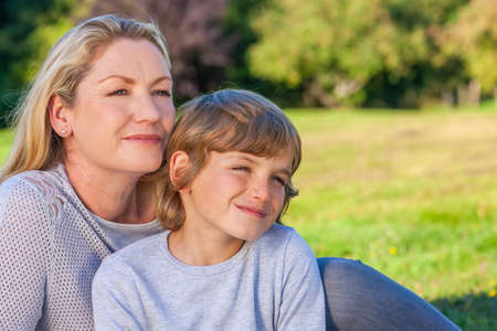Mother and son, boy child and woman, sitting together, smiling outside in summer sunshineの写真素材