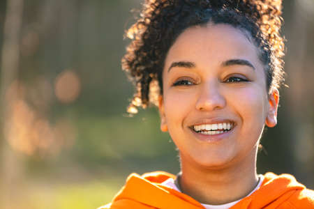 Outdoor portrait of beautiful happy mixed race biracial African American girl teenager female young woman smiling with perfect teeth wearing an orange hoodieの写真素材