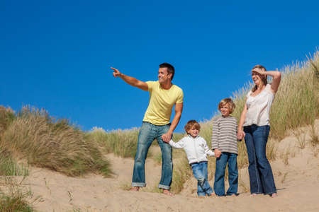 Happy family of mother, father and two sons, man woman children walking holding hands, having fun in the sand dunes of a sunny beachの写真素材