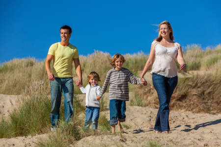 Happy family of mother, father and two sons, man woman children walking holding hands, having fun in the sand dunes of a sunny beachの写真素材