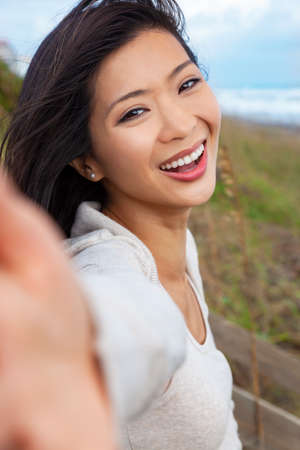 Outdoor selfie portrait of a beautiful happy fit healthy young Chinese Asian young woman or girl laughing with perfect teeth with natural backgroundの写真素材