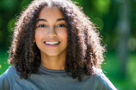 Outdoor portrait of beautiful happy mixed race African American girl teenager female young woman smiling with perfect teethの写真素材