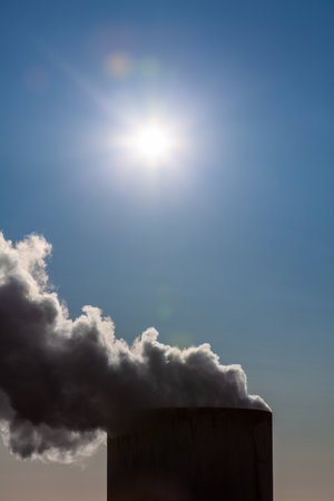 Climate change environmental pollution global warming concept smoke or steam coming out of chimney stack under the sun in a blue skyの写真素材