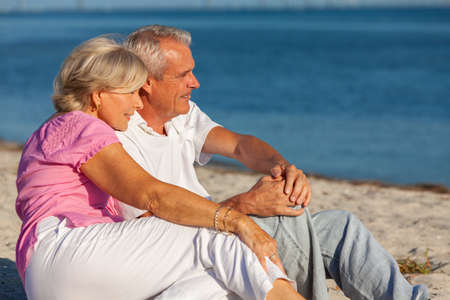 Happy senior man and woman retired couple sitting, smiling on a sunny beachの写真素材