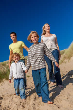 Happy family of mother, father and two sons, man woman children walking holding hands, having fun in the sand dunes of a sunny beachの写真素材