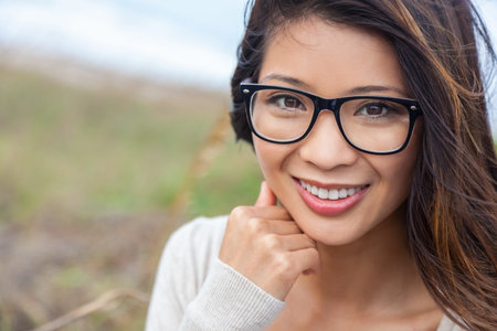 Portrait of a beautiful chinese asian girl or young woman with perfect teeth outside wearing glasses