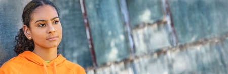 Panoramic header of beautiful mixed race African American girl teenager female young woman looking sad depressed or thoughtful outside in an urban city setting. Panorama web banner.の写真素材