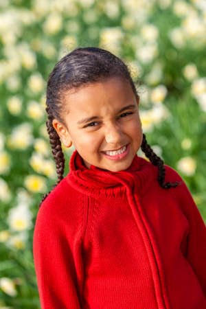 Beautiful young African American mixed race girl smiling and standing in a field of daffodilsの写真素材