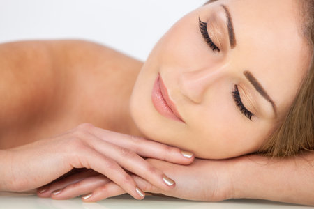 Portrait of a beautiful blond young woman with eyes closed or sleeping and resting on her handsの写真素材