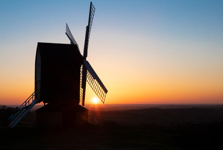 Sun setting on the horizon behind a traditional wooden British windmill at sunsetの写真素材