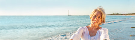 Panoramic web banner happy senior woman dancing and reaching with her hands on a deserted tropical beachの写真素材