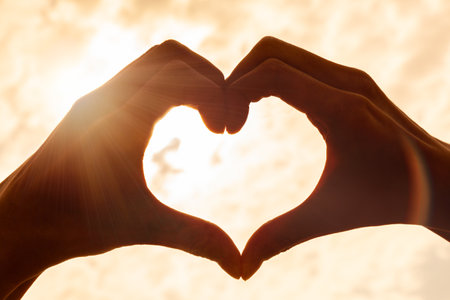 Hand heart shape silhouette made against the sun & sky of a sunrise or sunsetの写真素材