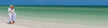 Panorama happy senior man and woman couple dancing and holding hands on a deserted tropical beach with bright clear blue sky panoramic web banner headerの写真素材