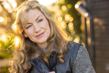 Attractive thoughtful middle aged woman outside smiling in golden hour sunlightの写真素材