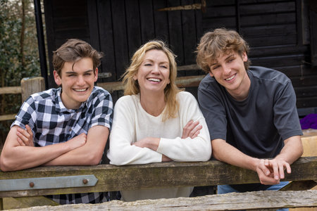 Family of mother and two teenage young men adult sons boys outside leaning on a fence laughing smiling happy togetherの写真素材