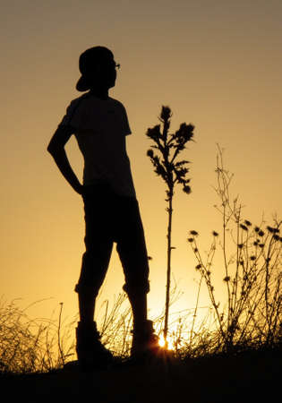 young man with his back to a beautiful sunset next to a plant with spikesの写真素材