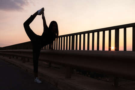 beautiful young brunette girl posing a road in the middle of the field at sunset, ballet, silhouetteの写真素材