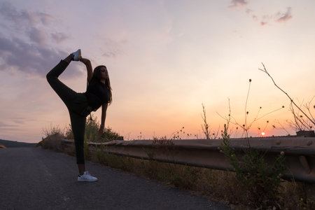 beautiful young brunette girl posing a road in the middle of the field at sunset, ballet, silhouette