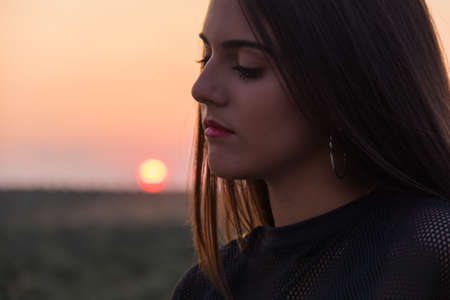 beautiful young brunette girl posing a road in the middle of the field at sunsetの写真素材