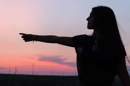 beautiful young brunette girl posing a road in the middle of the field at sunset, silhouetteの写真素材