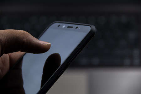 hand using a modern mobile and a laptop backgroundの写真素材