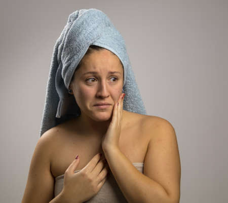 Girl after bathing with a towel and scared, points to the pimples on her faceの写真素材