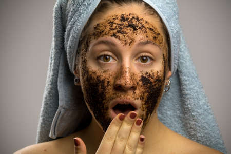 Portrait of unexpected shocked wondered model wrapped in towel with turban on head after shower towel, face with homemade coffee cream, isolated on white backgroundの写真素材